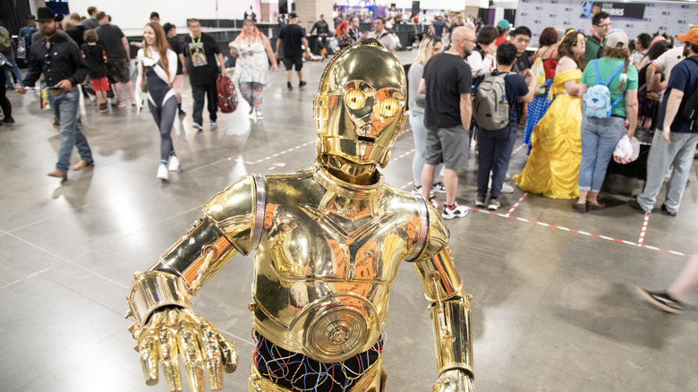 C-3PO poses for the camera as people stand in line and move around behind him