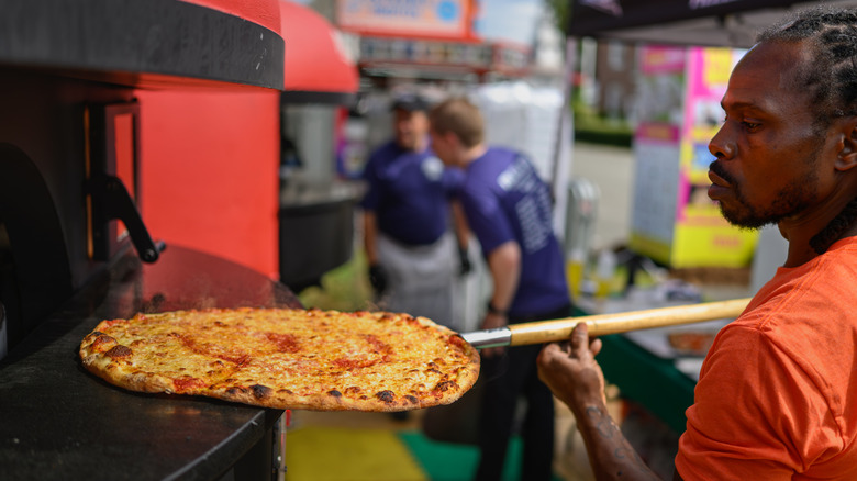 Dwayne Miller, a master cook with Frank Pepe's in New Haven checks on a pizza baking at The Big E. Kevin Galliard, who "Runs the operations for the Frank Pepe family," said the heart and soul of a Pepe's pizza is, "Fresh crushed tomatoes that we crush on site from Italy.