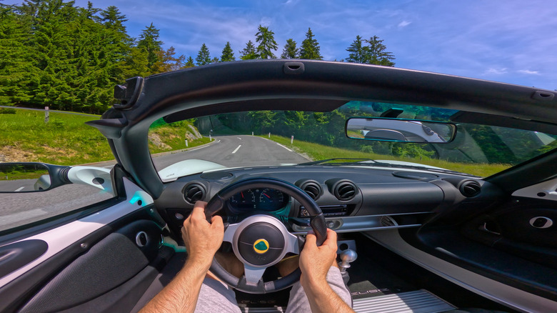 A driver behind the wheel of a Lotus convertible sports car