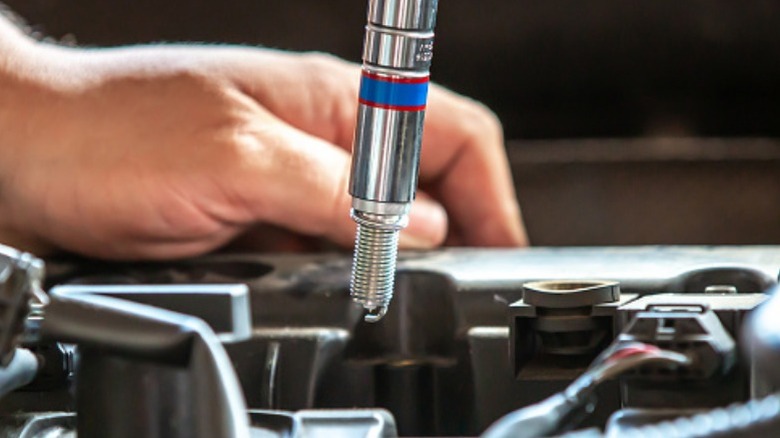 A person using a spark plug socket to install a new plug, showcasing the socket's ability to grasp a spark plug without the plug falling out.