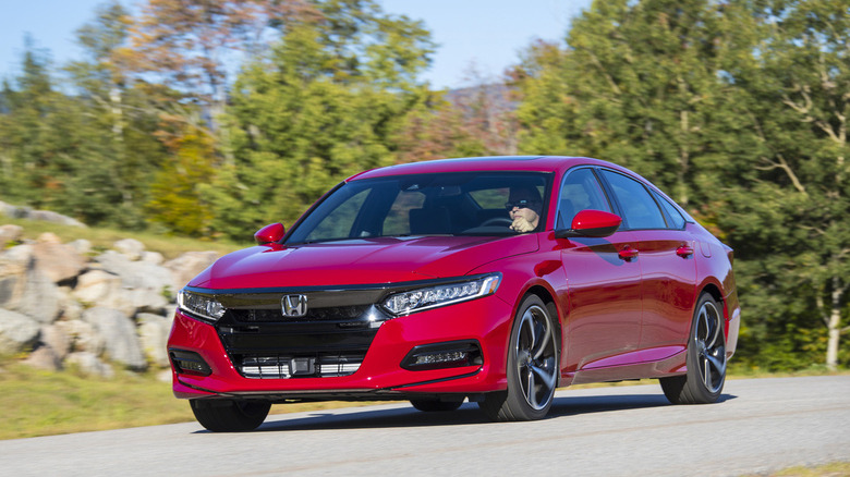 A vibrant red 2020 Honda Accord 2.0 T Sport sedan driving along a sweeping road, framed by rocky banks and green trees.