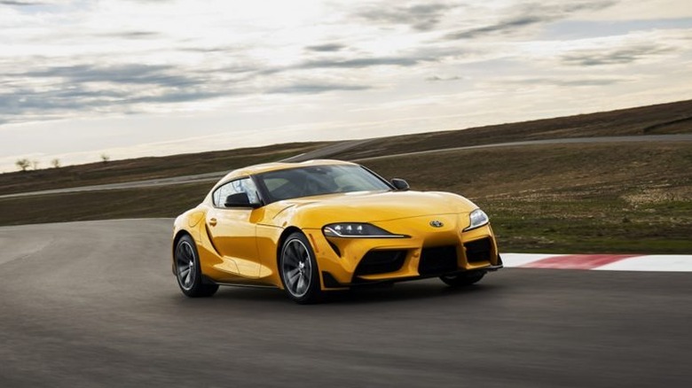 A bright yellow 2021 Toyota GR Supra 2.0 speeding through a curved section of an asphalt racetrack.