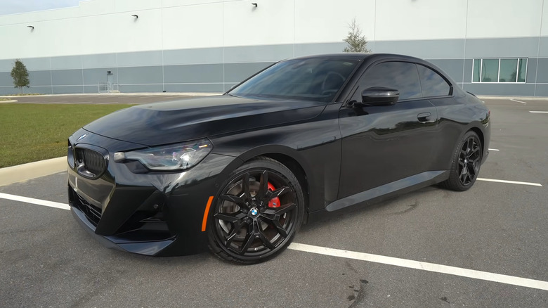 A modern gloss black BMW 230i Coupe parked in an empty asphalt lot.