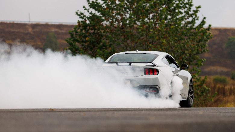 A light gray Ford Mustang EcoBoost with an RTR package executing a hard drift, with its rear end kicking up a thick, billowing plume of white tire smoke on a closed course.