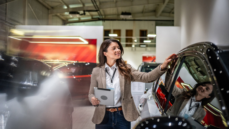 A woman with her hand on a car in a brightly-lit showroom