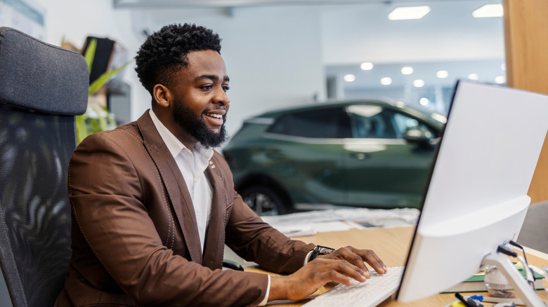 A man in a suit in a car dealership sitting at a desk and using a computer