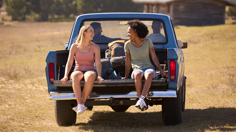 Women riding happily at the bed of a pickup truck.