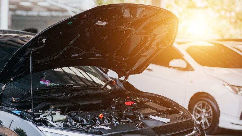 A car parked at a dealership with its hood open, sunlight in the background.