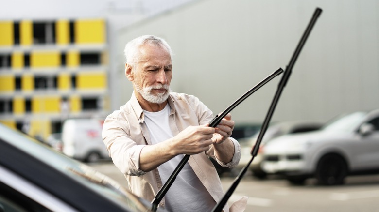 A man inspecting the windshield wipers on a car.