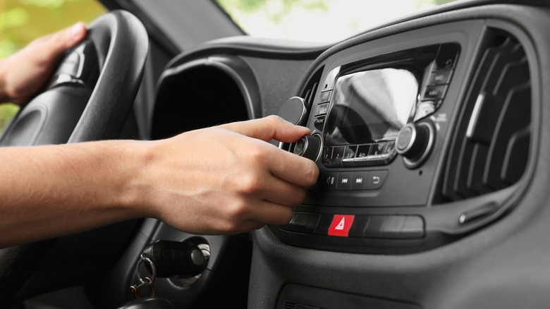 A person turning a radio knob in an older car