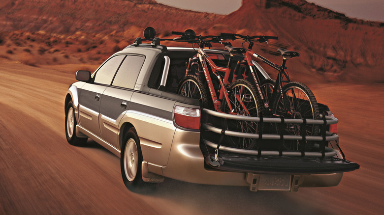 Two-tone gray Subaru Baja left rear view driving on a dirt road with bicycles in the back