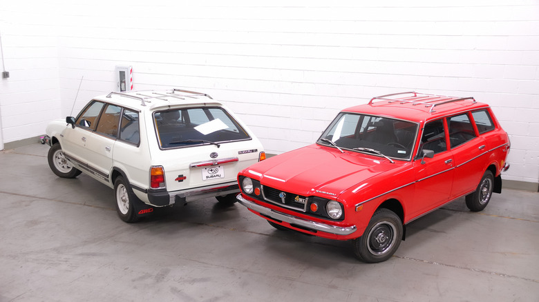Red 1976 Subaru wagon left front view and white 1980 Subaru GL wagon left rear view, both parked in a studio