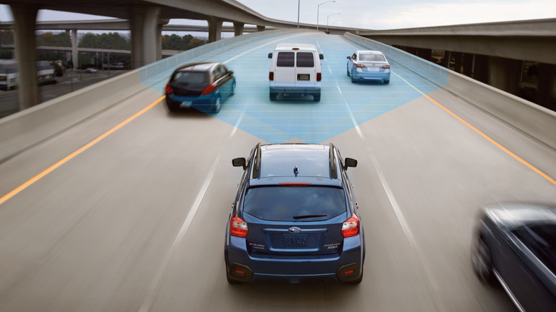 An overhead shot showing a blue Crosstrek driving in the middle lane of a freeway with three cars ahead and the EyeSight system's camera view is shown by a blue beam