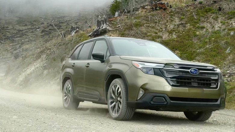 A front three quarters shot of a green Forester driving on a dirt path in front of green mountainside