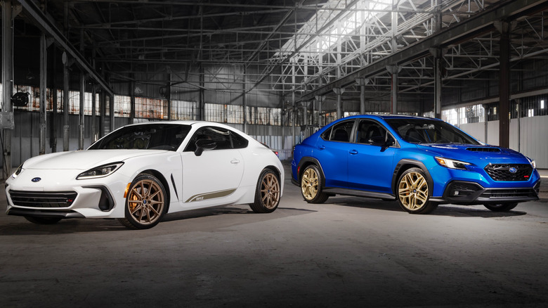 Front three-quarters shot of the white BRZ and blue WRX parked facing away from each other inside a very gray warehouse