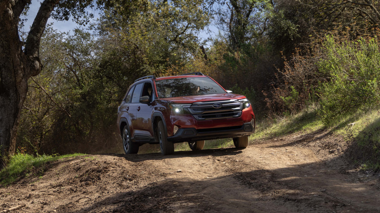 2025 Subaru Forester Hybrid drives along a dirt path surrounded by trees.