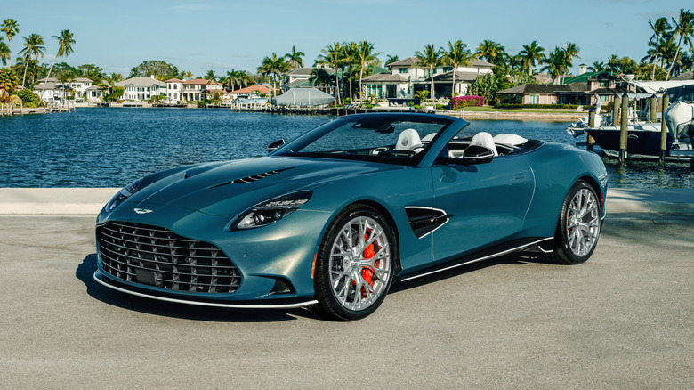 A teal "Wave Edition" Aston Martin Vanquish Volante convertible parked by a marina.