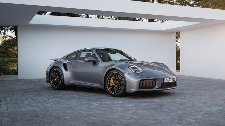 A silver Porsche 911 Turbo S Hybrid parked in a minimalist, modern driveway at sunset.