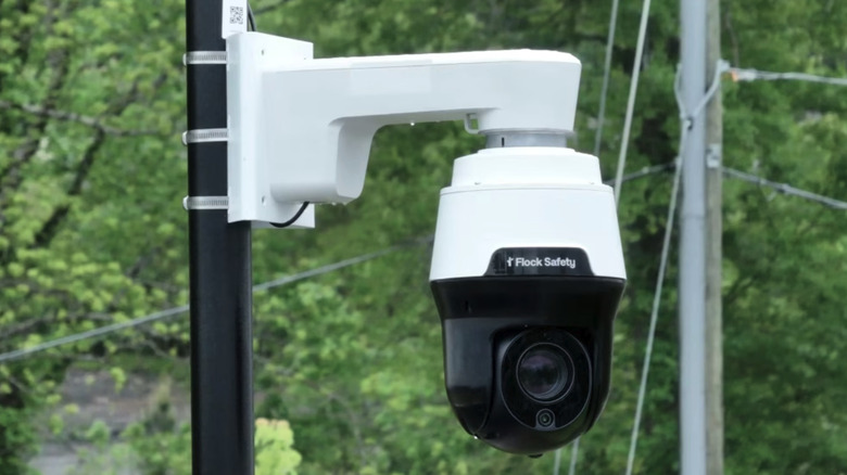 Close-up of a Flock Safety video camera strapped to a pole in a tree-lined neighborhood.