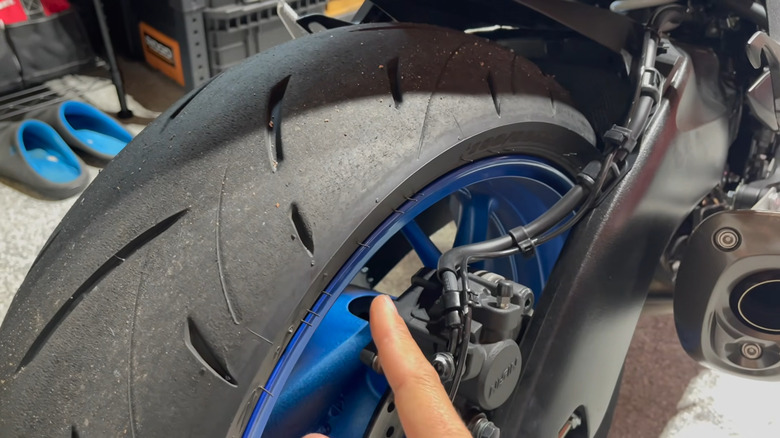 A finger indicates marking along the edge of a motorcycle tire in a garage.