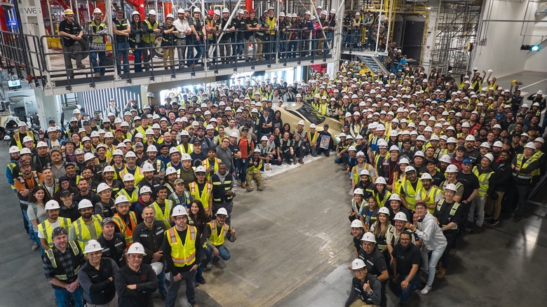 Workers in a Tesla factory crowd around a Cybercab