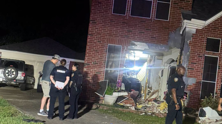 Cops surround a house where a Tesla sits inside, visible through a torn-down wall