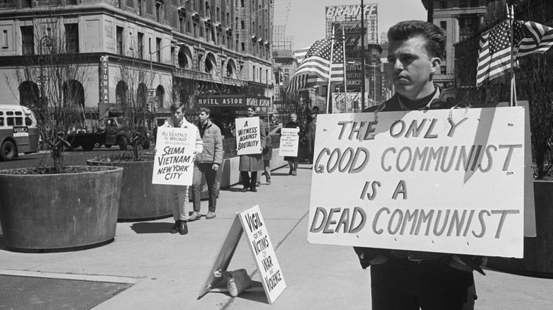 (Original Caption) 4/17/1965-New York, New York- Anti-Communist picket stands solidly opposed to young protesters maintaining a silent, shuffling vigil against violence in Times Square. In Washington nearly 15,000 students protested the U.S. "get tough" policy against the Communist guerillas in Vietnam.
