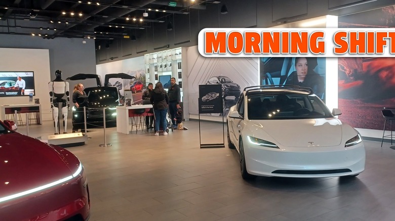 A red Tesla Model Y and a white Tesla vehicle are displayed inside a modern Tesla showroom.