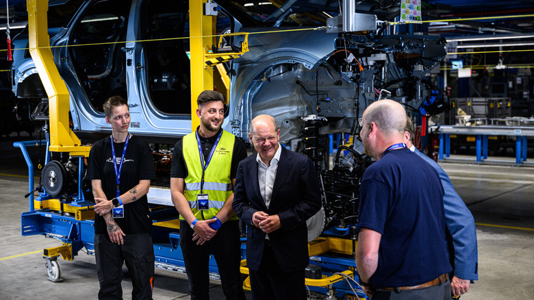 German Chancellor Olaf Scholz (C) and William Clay Ford Junior (R), Executive Chairman of Ford, chat with workers next to an electric Ford Explorer as they visit the electric car production line at the Ford automobile factory on June 12, 2023 in Cologne, Germany. Dubbed the "Cologne Electrification Center", the new factory hall is part of the plant's transition to increasing Ford's electric car production capacity.