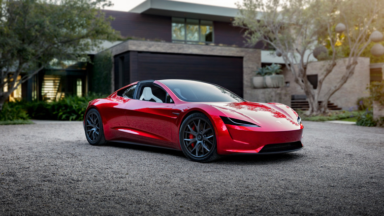 A red Tesla Roadster, seen in front three-quarter view in a driveway