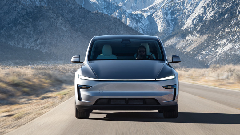 A silver Tesla Model Y driving with snowy mountains behind it