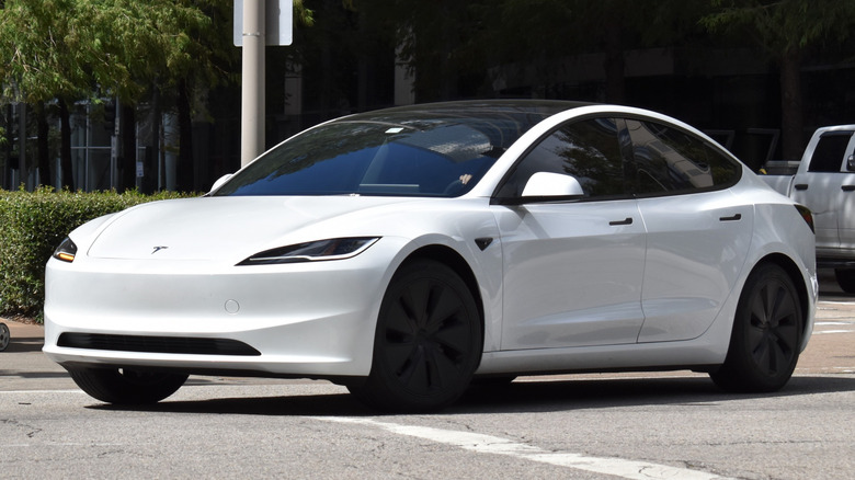 Houston, TX USA - 10/04/2024 - A portrait of a white Tesla Model 3 EV cruising in a downtown district