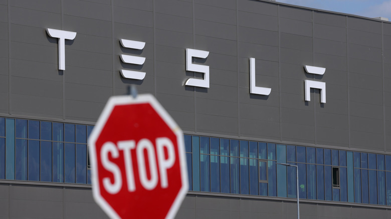 GRUENHEIDE, GERMANY - JULY 17: A stop sign stands near the Tesla logo at the Tesla factory on July 17, 2023 near Gruenheide, Germany. Tesla will reportedly present its plans tomorrow to expand production at the factory, from thee current level of approximately 250,000 cars per year to one million. The plan calls for the construction of a new assembly hall that will be the size of 60 soccer fields, which is likely to draw opposition from local communities.