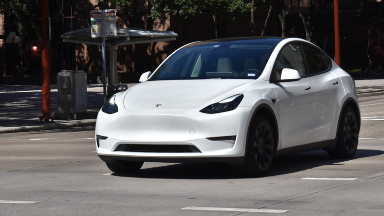 Front 3/4 view of a white 2024 Tesla Model Y driving on a city street