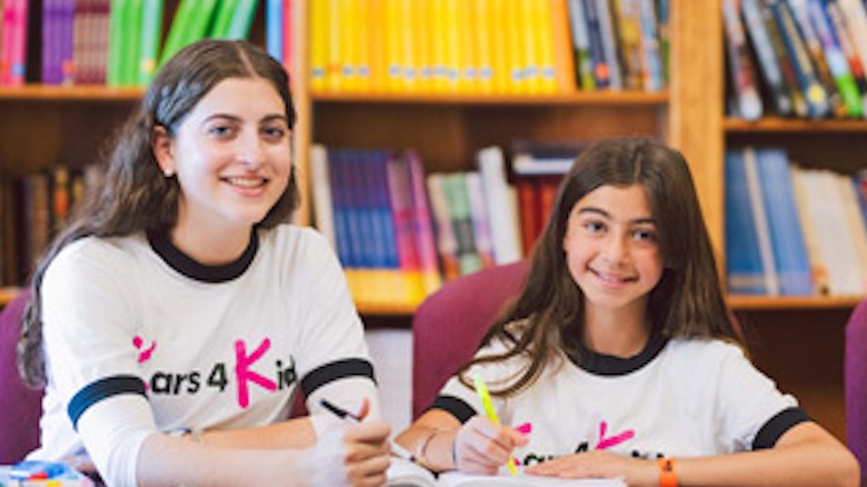 A young woman and a child sit at a desk wearing Kars4Kids shirts.