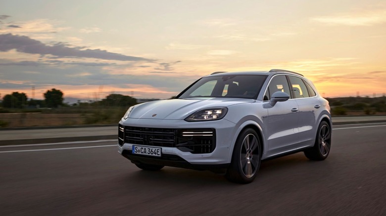 A white Porsche Cayenne Turbo E-Hybrid driving on a highway during a warm sunset.