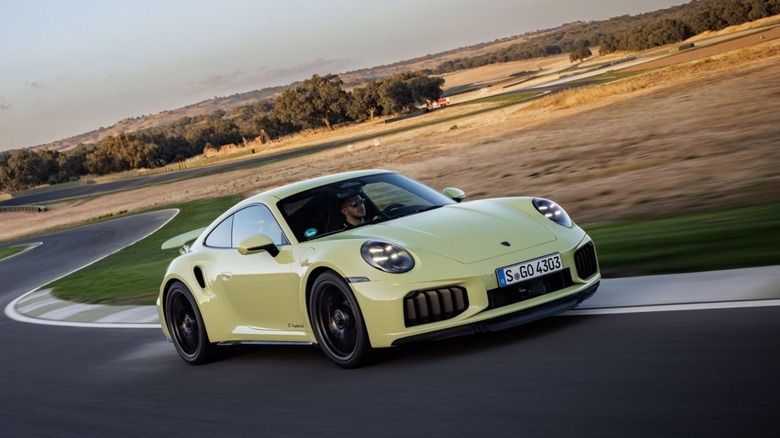 A vibrant Cartagena Yellow Metallic Porsche 911 Turbo T-Hybrid (992.2) cornering on a track.
