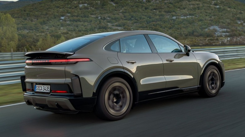 A Porsche Cayenne Turbo Coupe Electric in a muted olive-grey finish driving on a coastal road at dusk.