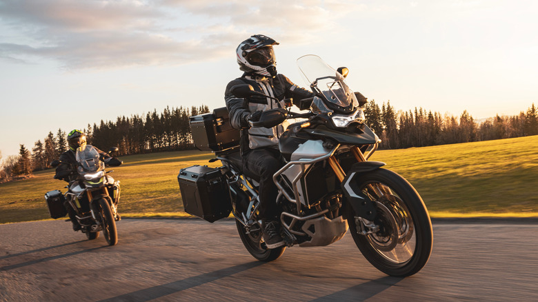 Two motorcycles ridden on an empty road on a sunny day.