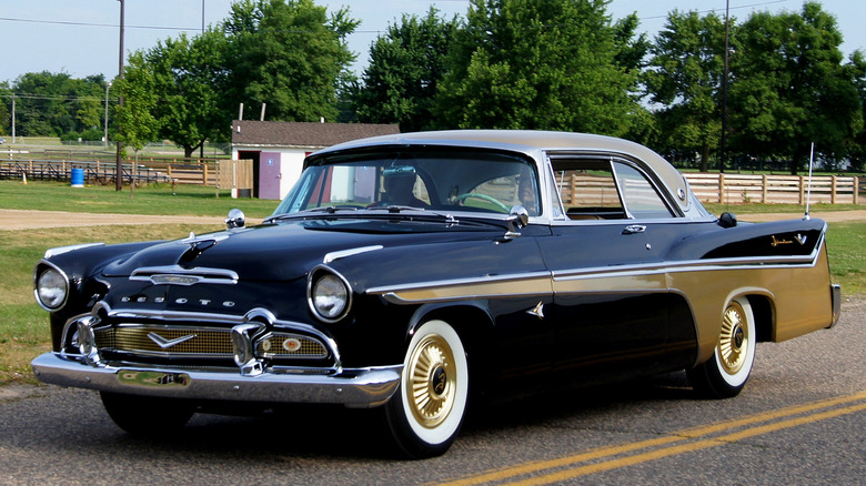A front 3/4 view of a black 1956 DeSoto Adventurer parked in front of a park