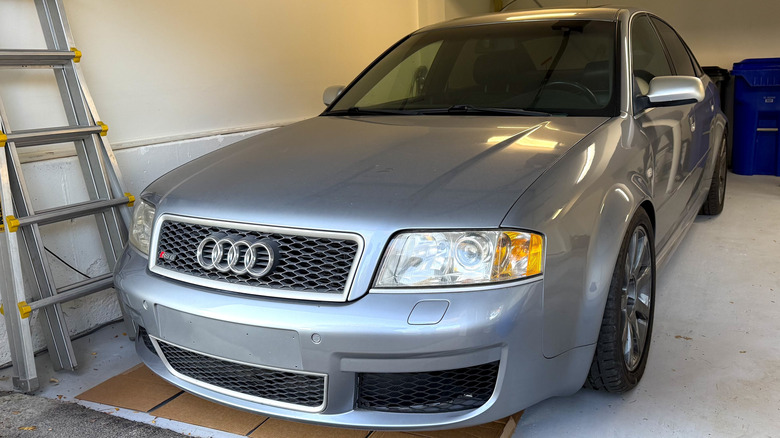 A grey C5-generation Audi RS6 sitting in a garage, with a latter pushed against the wall.
