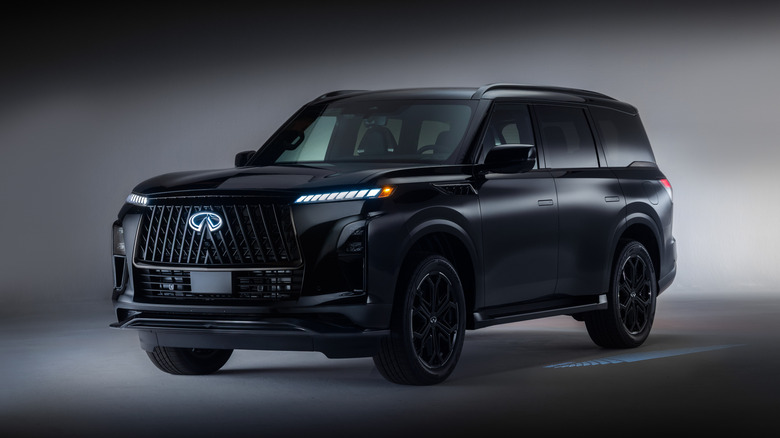 A blacked-out 2026 Infiniti QX80 Sport captured in a moody studio setting with an illuminated front emblem, sleek LED daytime running lights, and matching black wheels.