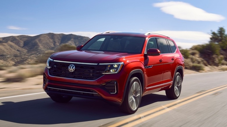 A bright red Volkswagen Atlas three-row family crossover driving down an open desert highway under a clear blue sky.