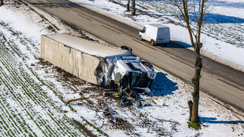 An overturned semi-truck on snow next to a road