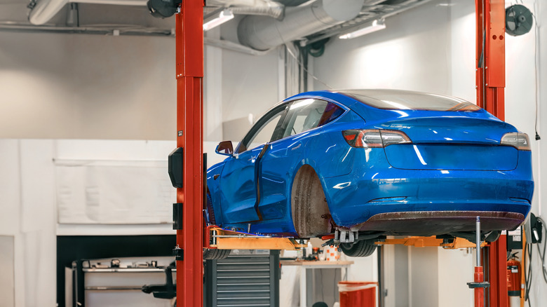 A blue Tesla EV on a repair lift with its rear wheels taken off.
