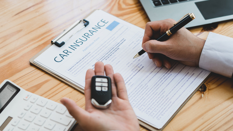 A person completes are car insurance application while holding a key.