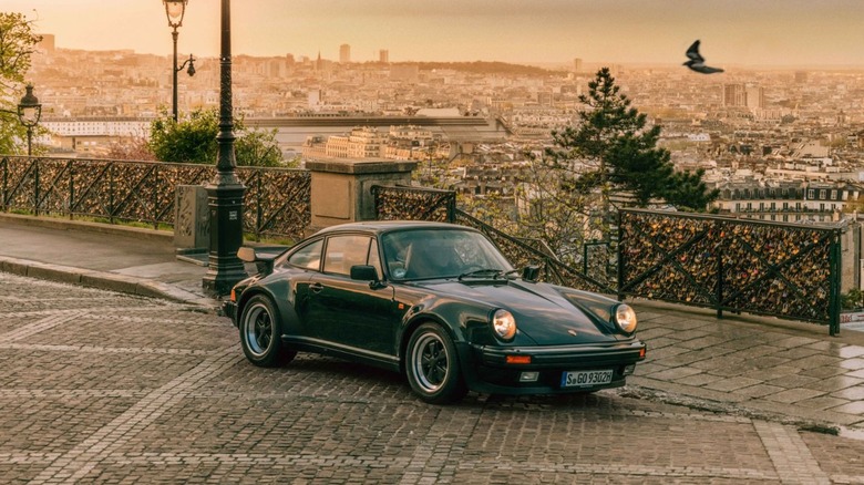 A front-quarter angle of a dark green Porsche 911 930 Turbo parked on a cobblestone street in Paris
