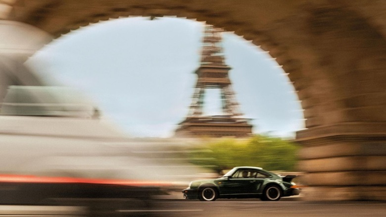 A side shot of a black Porsche 911 930 3.3 Turbo speeding through Paris with the Eiffel Tower in the background