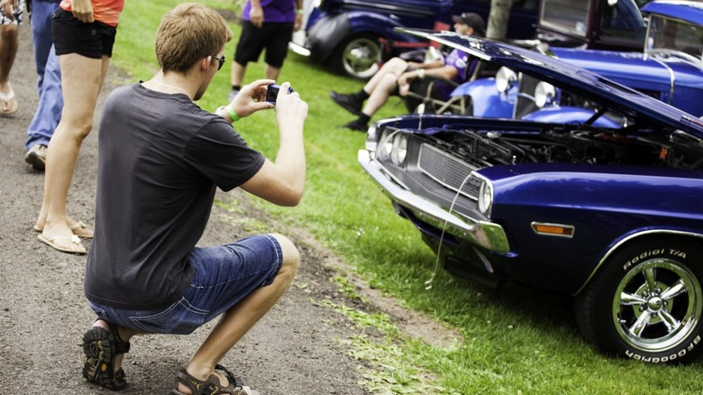 A person kneels to take photo of vintage Dodge Challenger at car show