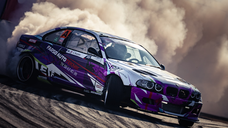 A purple-liveried E46 BMW M3 drifting and creating smoke.